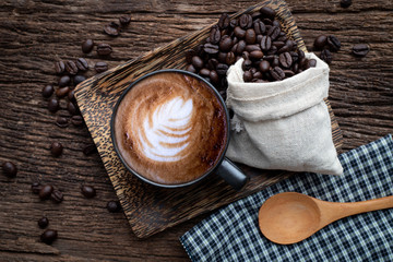 cup of latte coffee with coffee grains on wood table.