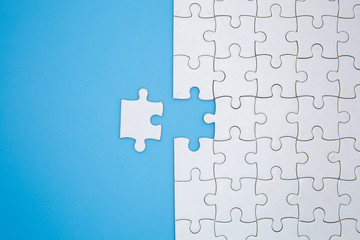 Unfinished white jigsaw puzzle pieces on blue background, The last piece of jigsaw puzzle, Copy space.