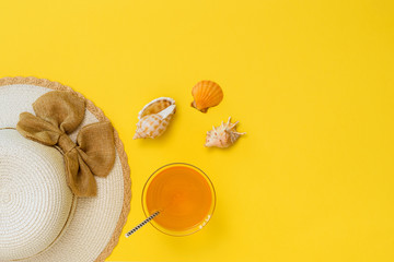 Three seashells, a hat and an orange drink on a yellow background. The concept of summer vacation. Flat lay.