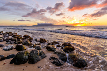 Tropical Sunset - A colorful sunset at a rocky beach of north-west coast of Maui island, with Lanai island at horizon. Hawaii, USA.