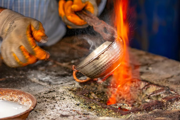 Cropped image of the traditional Turkish tinsmith covering the copper object with tin over fire. 