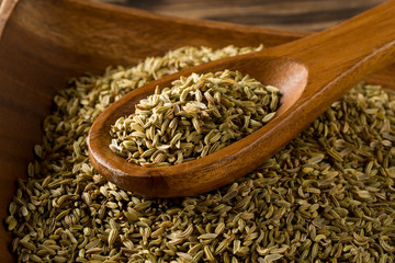 Dried fennel seeds in wooden bowl with wooden spoon on rustic wooden table background top view flat lay