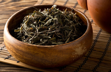 Dried, raw white tea leaves in wooden bowl on bamboo mat background
