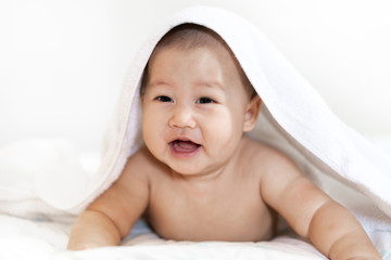 Portrait of happy smile baby relaxing under towel after bath on the bed