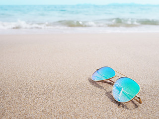 Fototapeta na wymiar sunglasses with blue lens on sand at sunset beach.