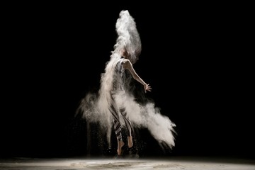 Graceful woman dancing in dust cloud in the dark