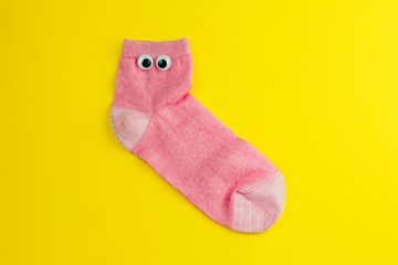 cute pink sock with googly eyes isolated on yellow background