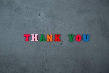 The multicolored Thank you word is made of wooden letters on a grey plastered wall background.