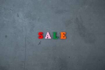 Fototapeta na wymiar The multicolored sale word is made of wooden letters on a grey plastered wall background.