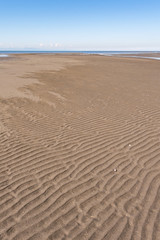 sandy beach on a clear day with wave ridge shaped patterns under clear blue sky on the coast