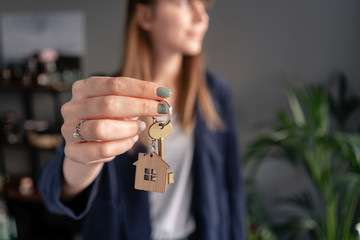 In the foreground house key in womans hands. Young pretty woman. Modern light lobby interior. Real...