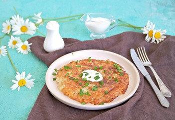 Roshty, fried potato pancake from boiled potatoes on a white clay plate on a turquoise background. Served with sour cream. Swiss cuisine.