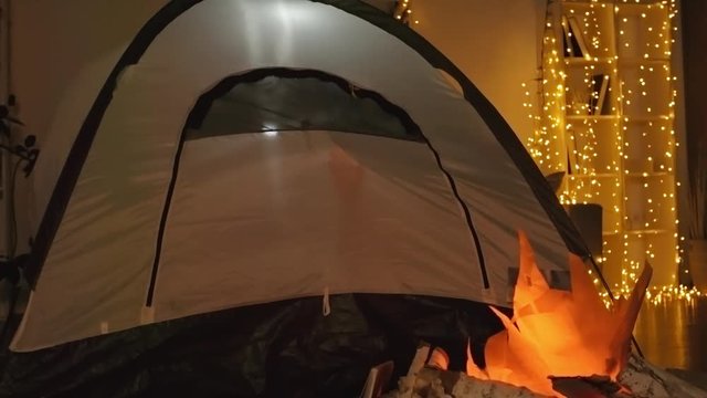 Time lapse of tent located in living room near artificial bonfire and kids silhouettes playing inside of it