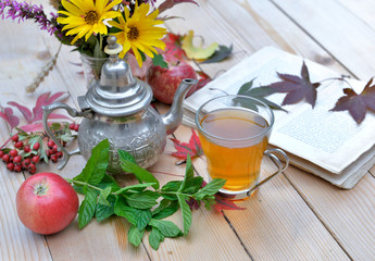 cup of mint tea  on a garden table with flowers and book for relaxing moment in autumn