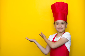 smiling girl in a red chef's suit points with both hands to a copy space on a yellow background