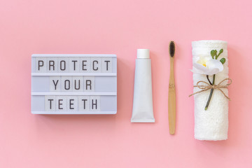 Protect your teeth text on light box and natural eco-friendly bamboo brush for teeth, towel, toothpaste tube. Set for washing on pink background. Concept dental health care Top view