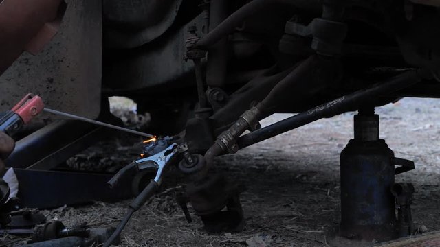 Hands of mechanic welding for repair the truck wishbone control arm of front wheel with dark and grain processed