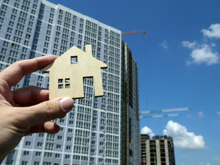 Hand holding symbol of property ownership in front of building.