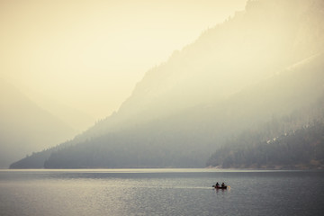 Fototapeta na wymiar Two people rowing a small boat on lake Plansee in the European Alps, in Austria at early morning sunrise