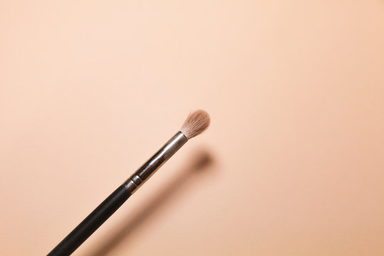 A makeup brush is pictured in front of a pink background