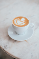 A cup of coffee with beautiful latte art in a white cup on marble table background.