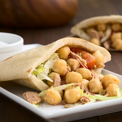 Pita sandwich stuffed with chickpea, tuna, lettuce, pepper, cherry tomato, roasted sunflower seeds on top, photographed with natural light (Selective Focus, Focus one third into the image)