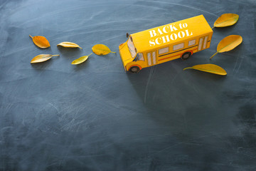 Back to school concept. Top view banner of cardboard school bus with autumn dry leaves over classroom blackboard background