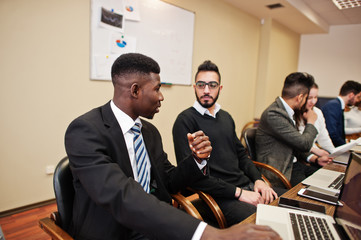 Multiracial business team addressing meeting around boardroom table.