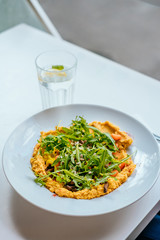 Bowl of carrot vegan hummus with chickpea, caramelized carrot, mashrooms, garlic, paprika, tahena, cumin, rocket salad and baked cauliflower. Glass of iced water with mint and lemon.