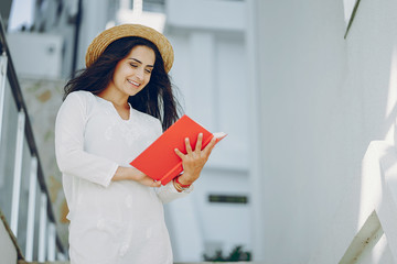 young and pretty girl in a summer city standing near stairs with red book