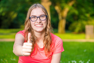 young woman holds her thumb up and smiles