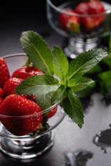 Fresh ripe red strawberries in a glass bowl on a black background