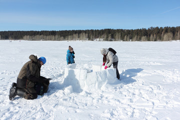 Happy grandfather, grandmother and grandson building an igloo on a snowy glade in winter