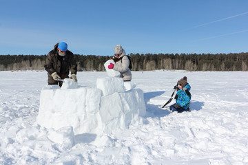 Happy grandfather, grandmother and grandson building an igloo on a snowy glade in winter,...