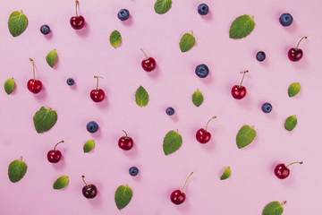 Green leaves, cherries and blueberries on pink surface
