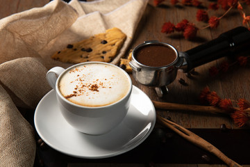 A cup of hot coffee cappuccino  with coffee bean, group handle, cinnamon and homemade cookie on wooden table