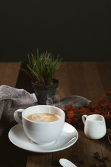 A cup of hot coffee  with coffee bean and milk cup on wooden table