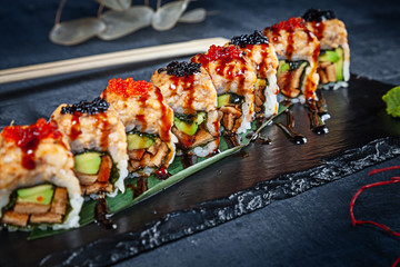 Close up view on set of sushi roll. Spicy roll with eel, avocado and caviar served on black stone on dark background. Japanese cuisine. Copy space. Served sushi for menu. Healthy food, seafood