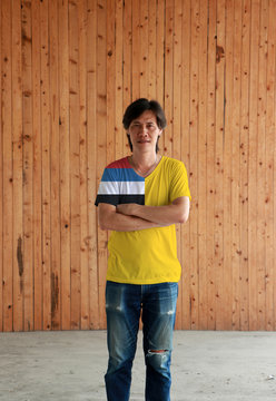 Man wearing Manchukuo flag color shirt and cross one's arm on wooden wall background.