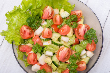 Delicious salad of vegetables, turnips, cucumber, tomato, avocado and parsley on a white background