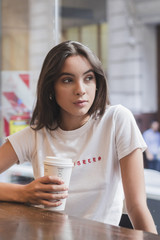 Portrait of a young woman sitting in cafï¿½ holding takeaway coffee cup in hand looking away