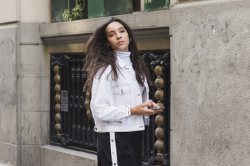 Stylish young woman holding mobile phone in hand looking at camera