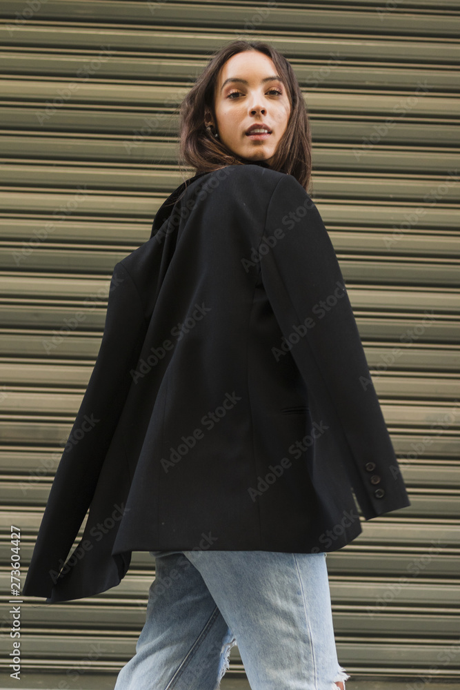 Wall mural Smiling young woman with black jacket standing in front of iron shutter