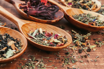Black tea with herbs in wooden spoons on a wooden board