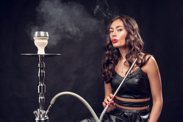 Fototapeta na wymiar girl smokes hookah / beautiful glamorous girl in black dress smokes a hookah