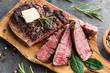 Medium rare Ribeye steak with herbs and a piece of butter on the wooden tray.