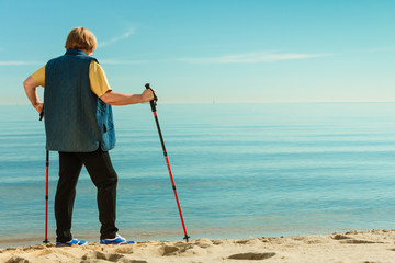 Senior woman practicing nordic walking on beach