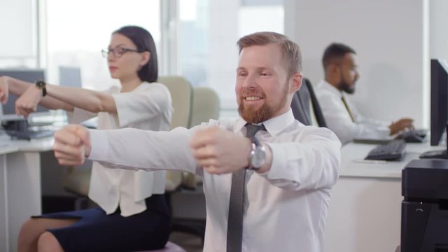 Lockdown of Caucasian businesswoman and businessman sitting, doing physical exercises while their colleague working on background