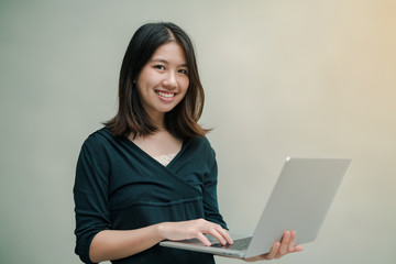 Closeup Asian beautiful woman Wearing a black shirt standing around the gray wall Use a laptop computer to work happily.