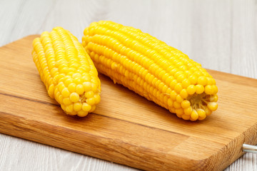 Cutting board with boiled corn on table.
